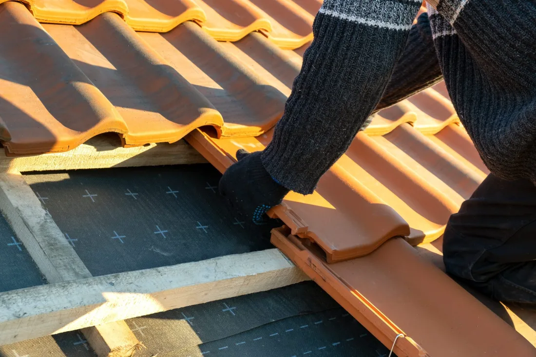 Roofer fitting new clay roof tiles over a breathable membrane